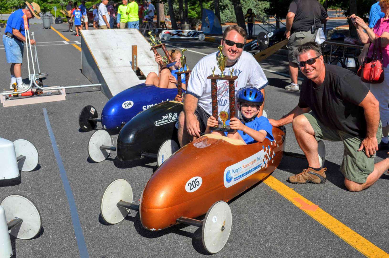 boy holding trophy in soap box derby car